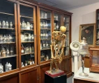 An unusually crafted skeleton against the backdrop of a 200-year-old English pharmacy cabinet containing almost 300 flasks